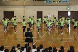 黄緑色のシャツを着た、三角小学校の3年1組の生徒が、市長と、在学生の前で踊っている写真