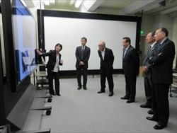 株式会社KDDI研究所訪問時に無響室での実験の説明を立って聞いている市長たちの写真