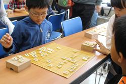 将棋の対戦をしている、眼鏡をかけた男児が駒をどこに置こうか考えている写真