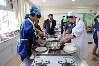 三角巾をかぶり体操服姿の中学生が料理をしている所を見ている市長の写真