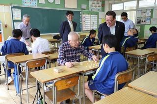 対面に座り将棋をしている中学生と白髪の男性を横で見ている市長の写真