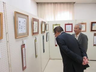 壁に展示されている書を、白髪の男性と一緒に見ている市長の写真