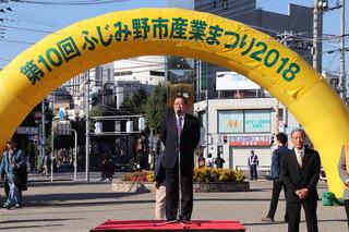 第10回ふじみ野市産業まつり2018と書かれているバルーンの前で、市長が台の上に立って話をしている写真