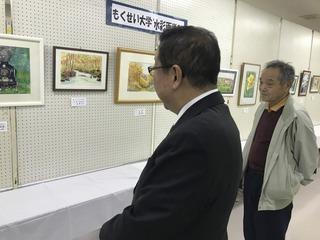 額に入った絵画が展示されており、市長とジャンパー着た男性が作品を見ている写真