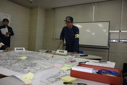 総合防災訓練で、机の上に広げられた地図の上を市長が棒を使って1点を指している写真