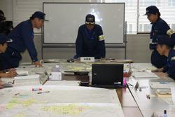 机にの上には、地図が広げられており、市長と関係者の方々が地図を見ながら話合いをしている総合防災訓練の写真