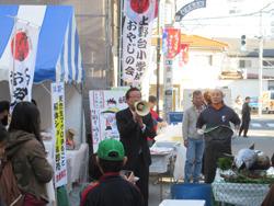 大楽市の行われている賑やかな上福岡駅前名店街の通りにて、市長が拡声器を持って話をしている写真