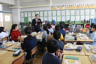 給食の時間に教室の後ろで話をしている市長を見ている子供達の写真
