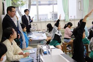 手を挙げている生徒達を、教室内の後方から見ている市長の写真