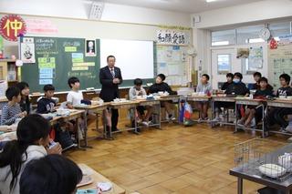 教室いっぱいに机を円に並べ座っている子供達に話をしている市長の写真