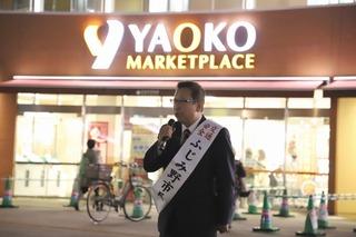スーパーマーケットの前の路上でたすきをかけてマイクを持ち、話をしている市長の写真