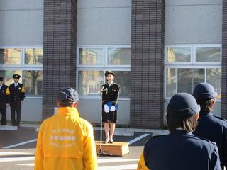 一日警察署長の飯田 里穂さんが台の上に上がりスタンドマイクにむかって挨拶をしている写真