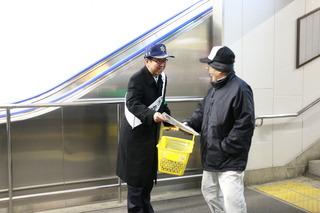 駅のホームから出てくる人に、市長が防犯キャンペーンのチラシを手渡ししている写真