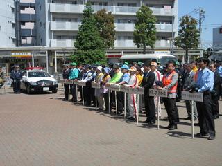 春の全国交通安全運動出陣式にてプラカードを持った団体が整列している奥にパトカーが写っている写真