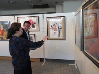 壁に飾られている作品を見ながら女性が話をしており、市長が聞いている写真