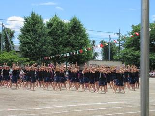 ダンスの演技が行われており、黒いティーシャツを着た児童達が右手をこぶしにして突き上げ左手を右手の肘に交差したポースを取っている写真