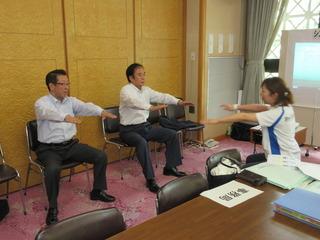 市長と上田 清司埼玉県知事が椅子に座って両手を肩の高さに挙げており、インストラクターの女性と体操をしている写真