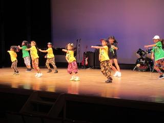 黄色と緑のシャツを着たキッズが舞台上でダンスをしている写真
