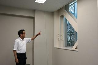 白の鉄骨の奥のガラスの窓を指さしている市長の写真