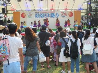 おおい祭りの舞台で小さな子供達がダンスを踊っている様子をみている来場者の人達の写真
