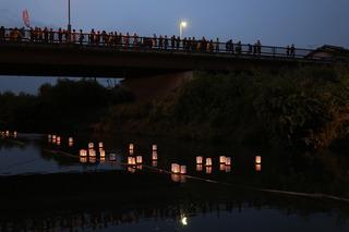 灯りのついた灯篭が川に流されている様子を橋の上から見ている参加者の写真
