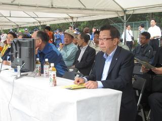 テントのテーブルに座って九都県市防災訓練を見ている市長の写真