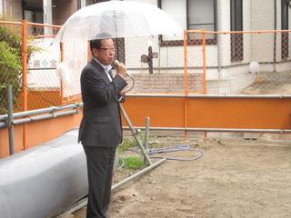 雨の中市長が傘をさしてマイクを持ち話をしている写真