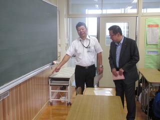 真新しい教室の黒板の前で、市長が関係者の男性から説明を受けている写真