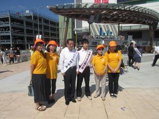 オレンジ色の帽子とティーシャツを着た女性4人と市長と男子学生が一緒に写っている写真