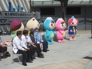 交通安全フェアの会場にて、ふじみんとゆるキャラの人形達が並んでおり、関係者の方と市長がパイプ椅子に座っている写真