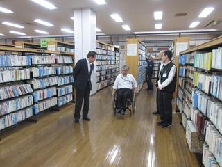 本棚の間が広いスペースになっており、車椅子に乗った男性と市長が話をしている写真
