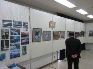 写真がボードに展示されており、市長が作品を見ている写真