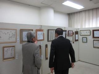 書の作品が展示されており、白髪の男性と市長が一緒に作品を見ている写真