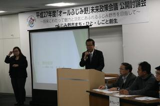 公開討論会の壇上で話をしている市長とその横で手話通訳をしている女性、関係者の人達の写真