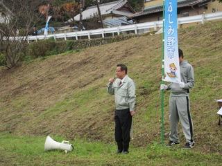 新河岸川でふじみ野市とかかれた旗を持つ人の前で挨拶をしている市長の写真