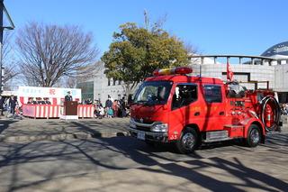 消防車の奥で消防出初式が行われている写真