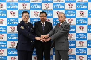市長と、警察職員、スーツの男性が、両手を交互に重ねている写真