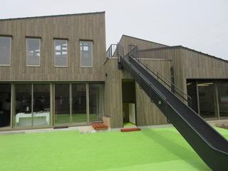 大きな窓にこげ茶の外壁、黒の滑り台が印象的なふじみの緑保育園の外観の写真