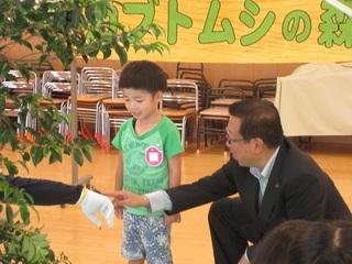 スタッフの手に乗っているカブトムシを指さす市長と見ている小さな男の子の写真