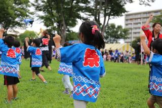 祭と背中にロゴの入った青い法被を着て踊っている小さな子供たちの写真