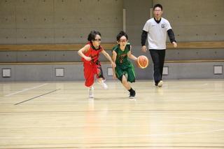 赤と緑のユニフォーム姿でバスケットをしている2名の男子選手の写真