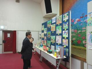 子供たちの「絵」や「工作」が展示されているブースを見学している市長の写真