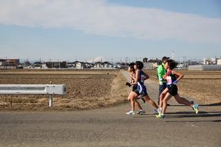 田んぼが広がっている中の道路を選手4名が競いながら、力走している様子の写真