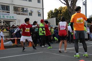 中継地点にて、前走者が次走者にバトンを渡しており、手前には前走者が走ってくるのを待っている様子の選手が2名が立っている写真