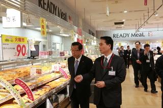 イオン大井店の食品売り場を歩きながら、スーツを着ている男性から市長が説明を聞いている写真