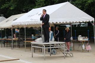 グランドにテントが立てられており、市長が朝礼台の上に立って、スタンドマイクの前話をしている写真