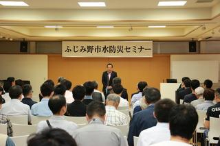 「ふじみ野市水防災セミナー」と書かれている横断幕の前で市長が話をしており、沢山の参加者が席に着いて話を聞いている様子の写真