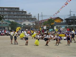 黄色いハチマキを頭に締めたけた児童達が黄色いボンボンを持って旗を元気よく振っている写真