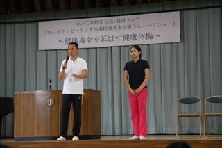 講師の方、男女2名舞台の上に立っており、白いポロシャツを着た男性がマイクを持って話をしている写真