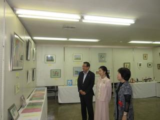 ふじみ野市文化美術連合会工芸部合同展に展示されている絵画を、市長とピンク色の洋服と黒い洋服を着た女性2人と見ている写真
